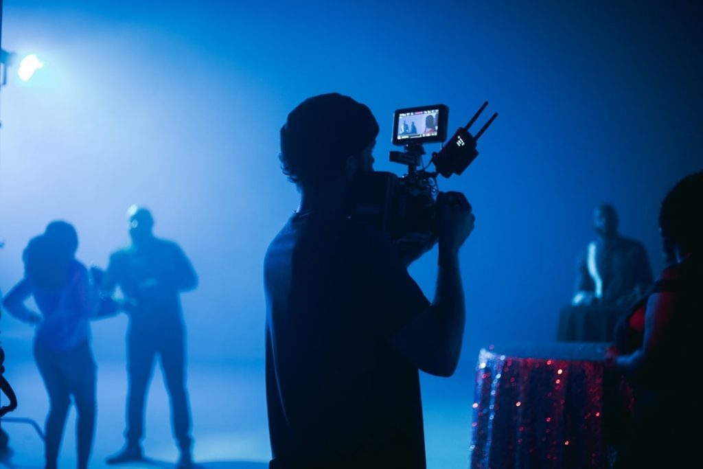 Silhouettes of a videographer filming an artist against blue light